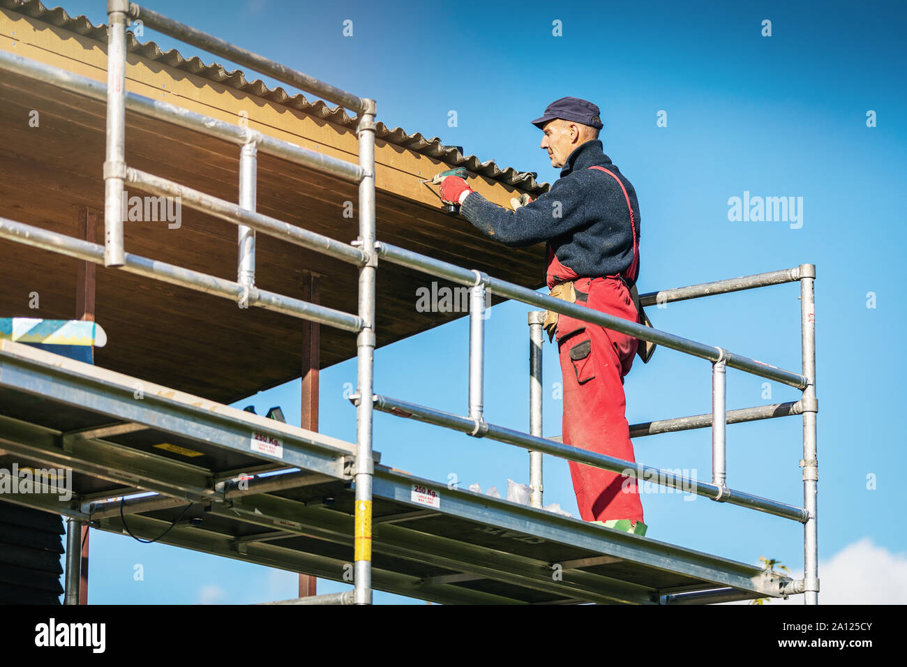 man on scaffolding installing new wooden planks on house roof eaves Stock Photo
