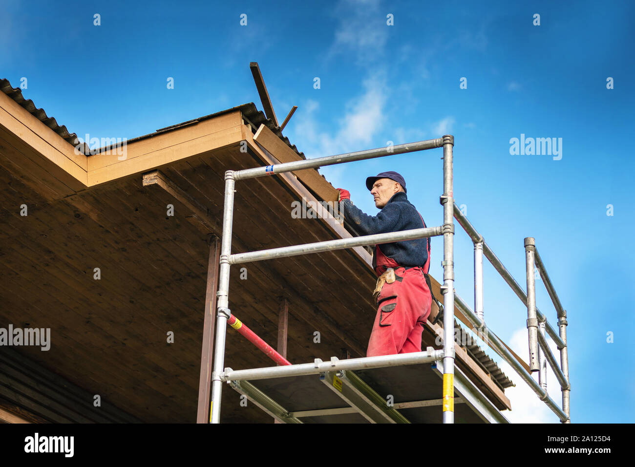 old house renovation - construction worker installing new planks on house roof eaves Stock Photo