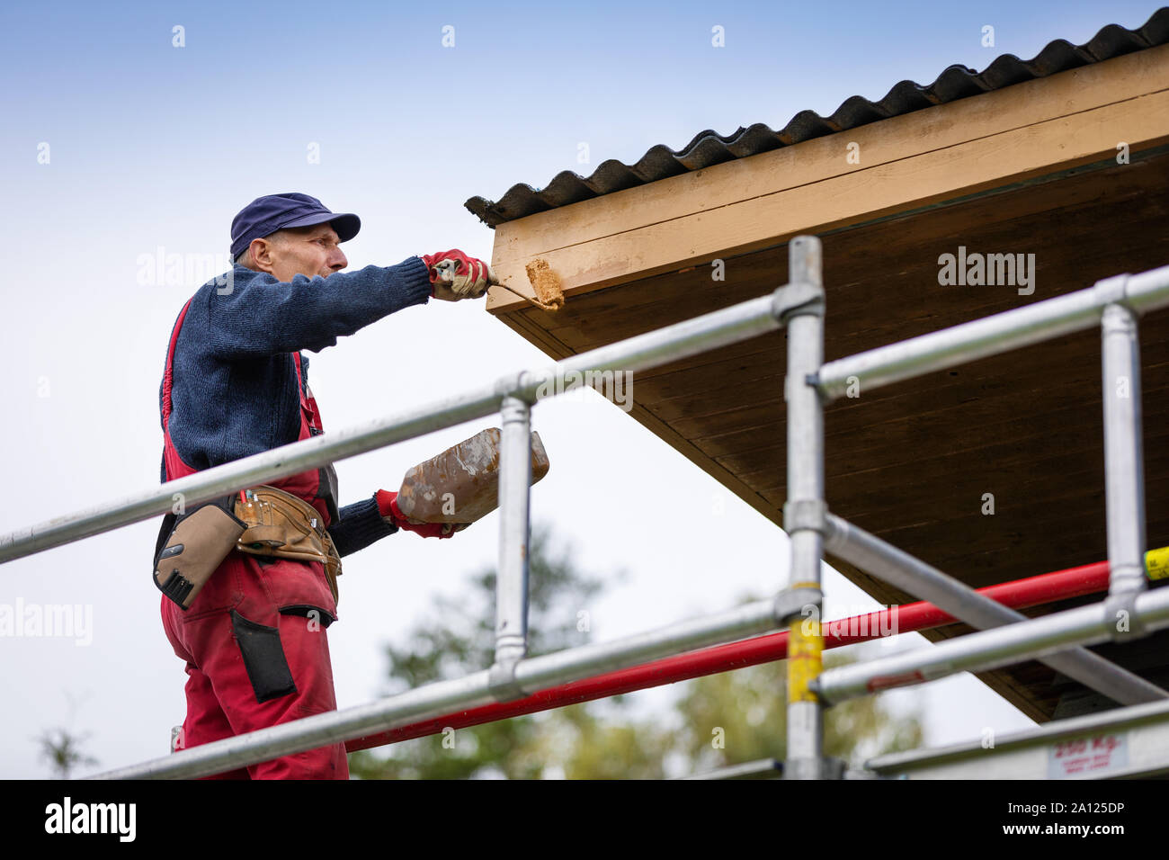 man on scaffolding painting house roof planks with paint roller Stock Photo