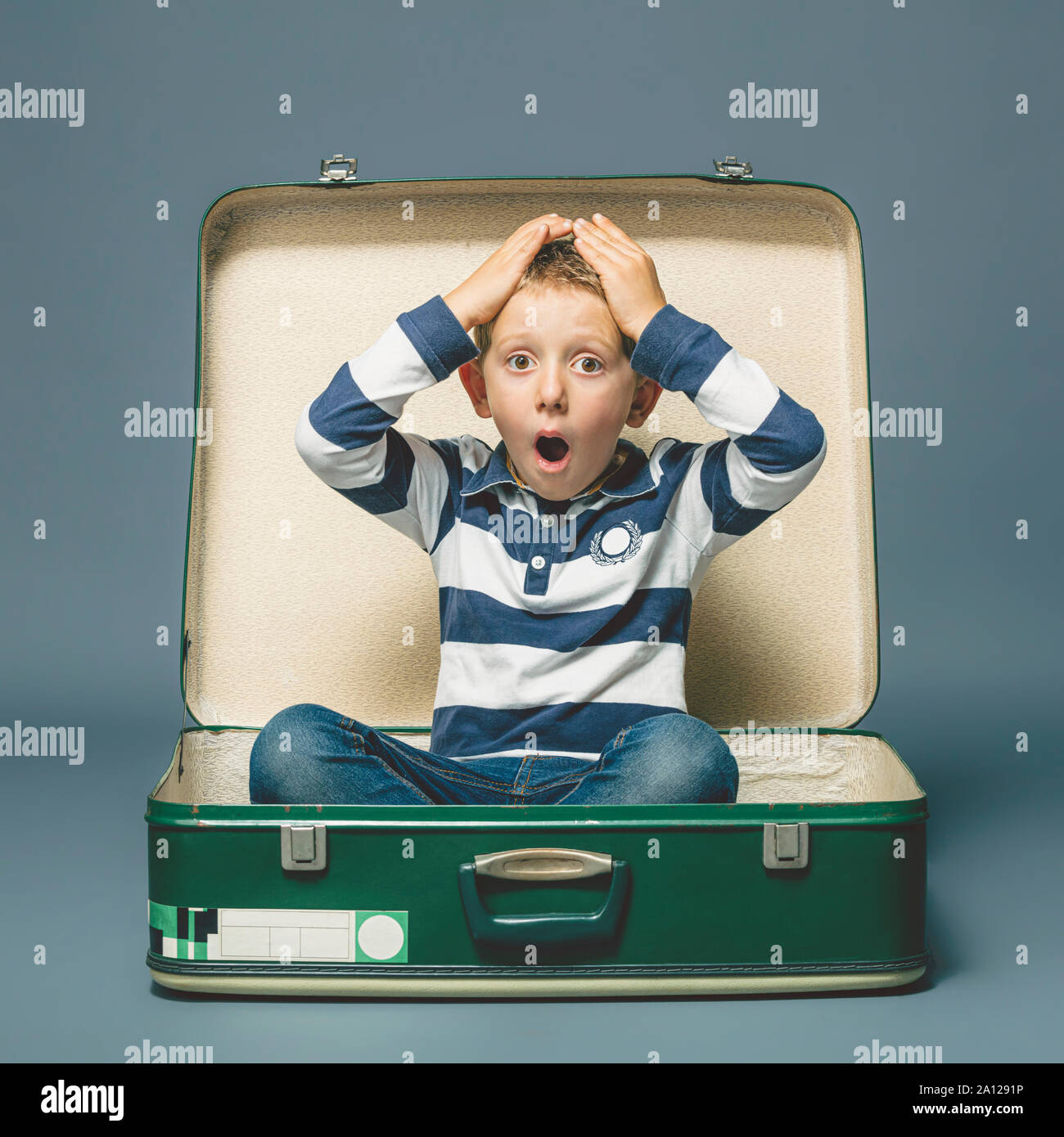 studio portrait of a 6 year old boy with a surprised expression sitting inside a vintage suitcase. Stock Photo