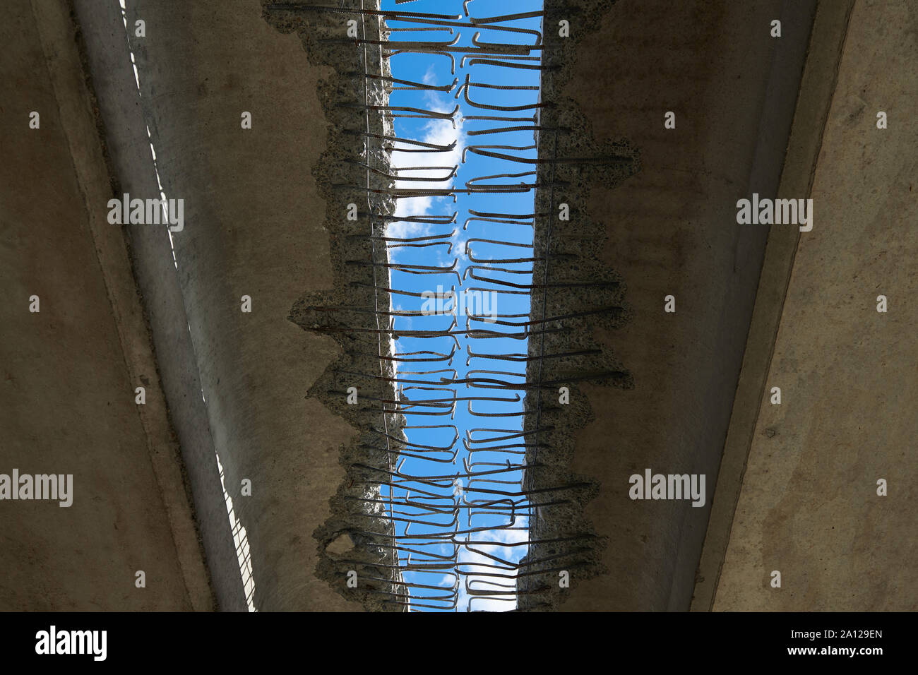 Under the bridge. Hole with a blue sky view. Abstract construction background. Metal rods in concrete. Old object under reconstruction. Stock Photo