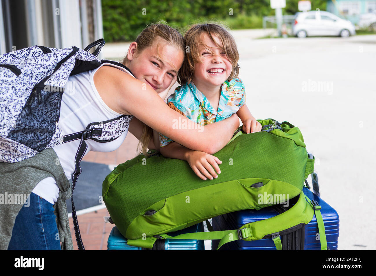 13 year old sister and her 5 year old brother leaning on travel luggage Stock Photo