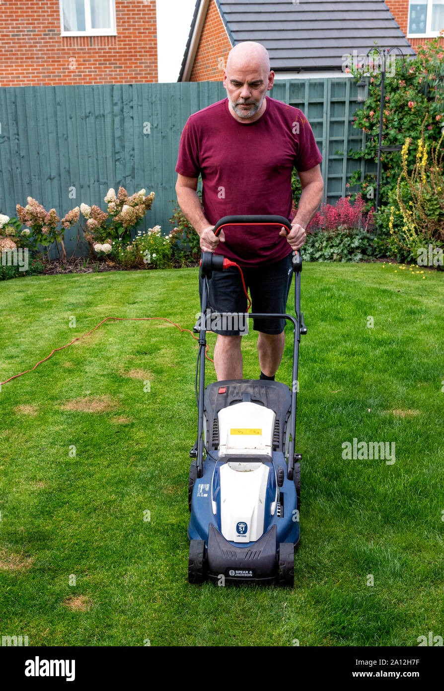 Man mowing his lawn with a Spear and Jackson electric lawnmower (facing front( Stock Photo
