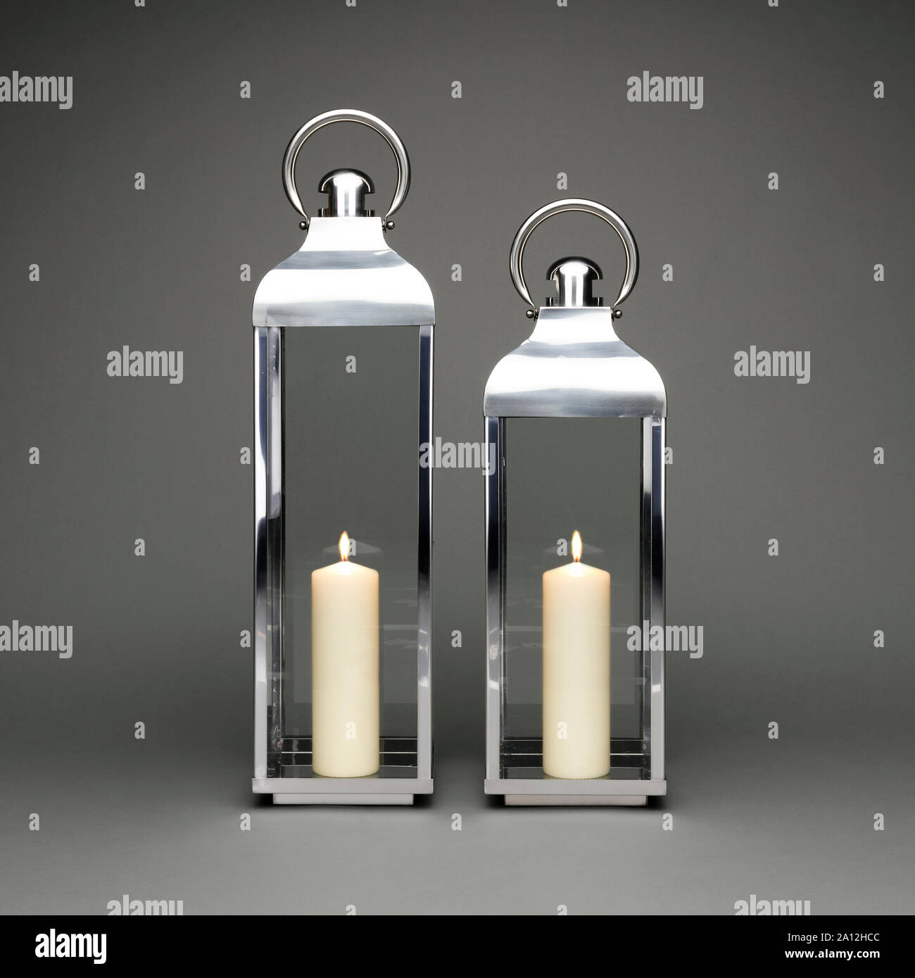 Two large candle holding lanterns, with lit candles on a dark grey