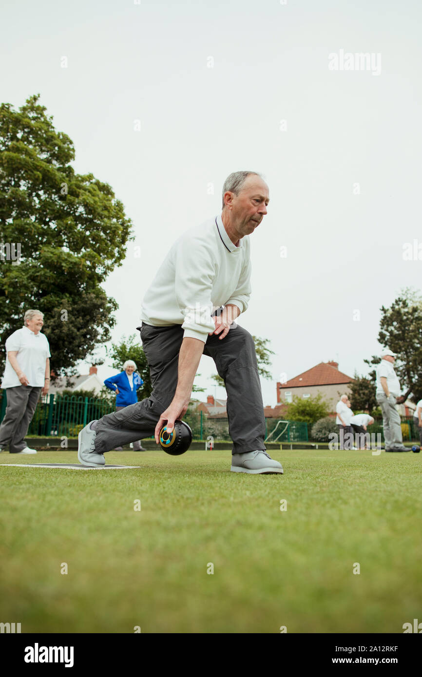 A front view shot of a senior man taking his shot in a game of lawn bowling. Stock Photo
