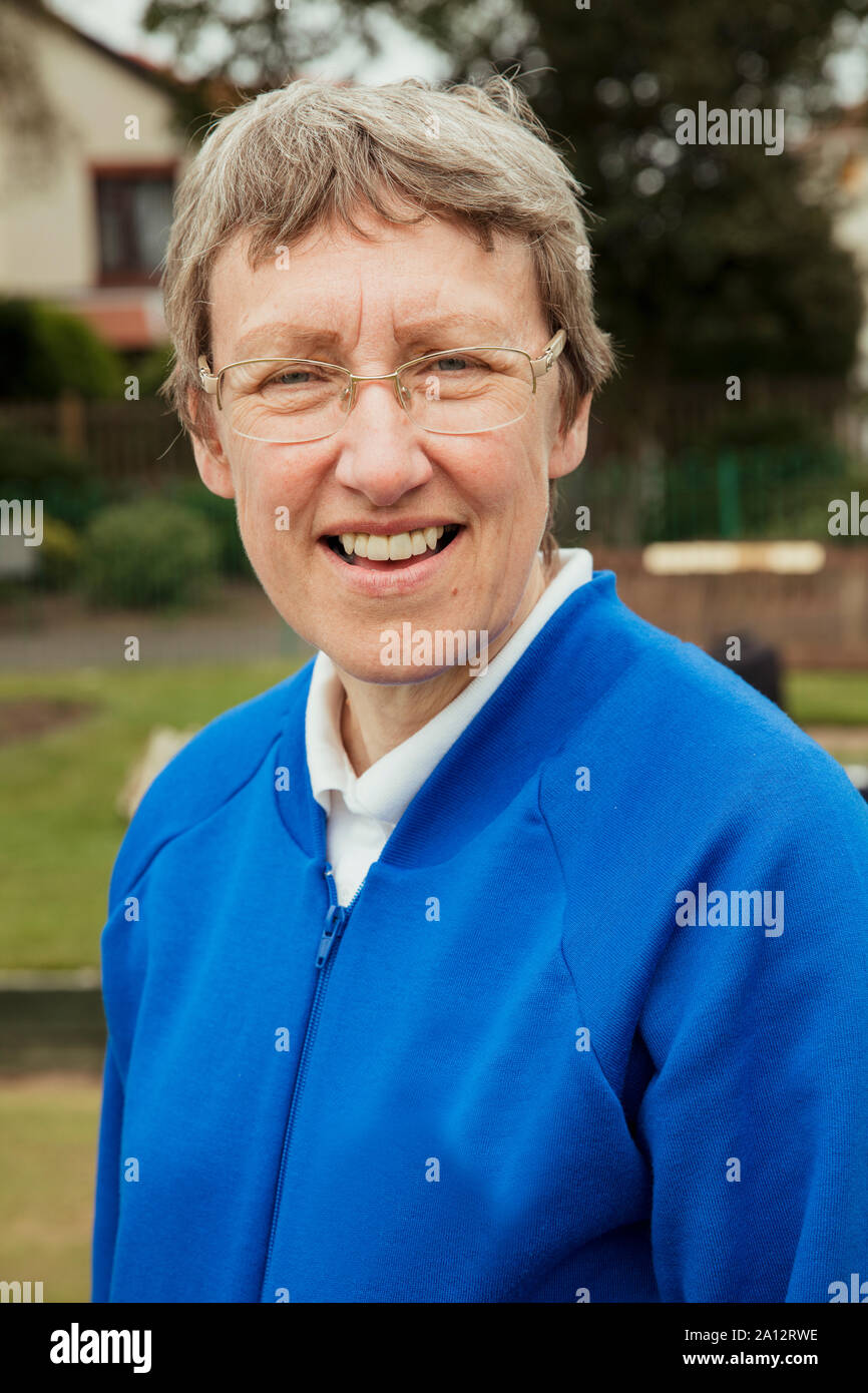 A portrait of a senior woman smiling at a bowling green. He is wearing glasses. Stock Photo