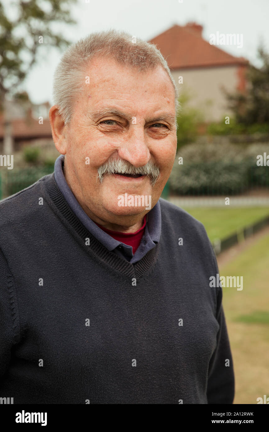 A portrait of a senior man with a moustache smiling at a bowling green. Stock Photo