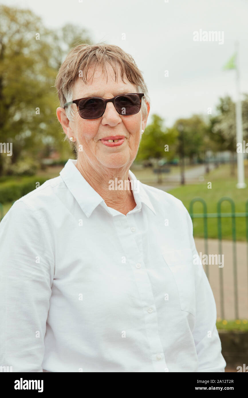 A portrait of a senior woman smiling at a bowling green. She is wearing sunglasses. Stock Photo