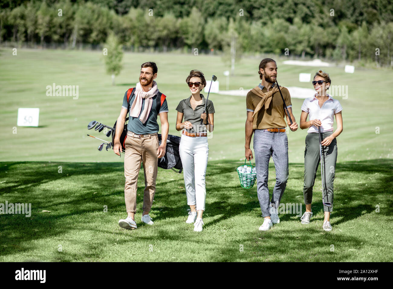 Young and elegant friends walking with golf equipment, hanging out together before the golf play on the beautiful course on a sunny day Stock Photo