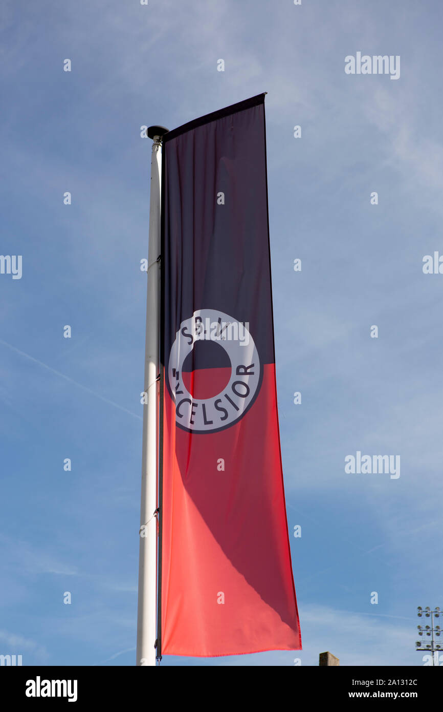 Flag of the Dutch soccer club Excelsior blowing in the wind against a blue sky with a lighting column of the stadium in the background Stock Photo