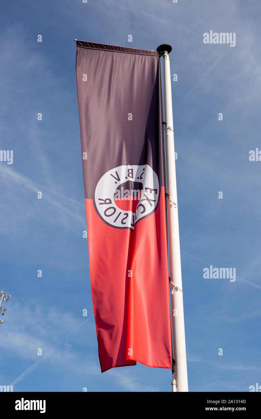 Flag of the Dutch soccer club Excelsior blowing in the wind against a blue sky with a lighting column of the stadium in the background Stock Photo