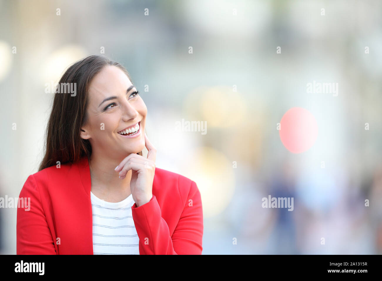 Front view portrait of a happy woman in red thinking looking at side outdoors in the street Stock Photo