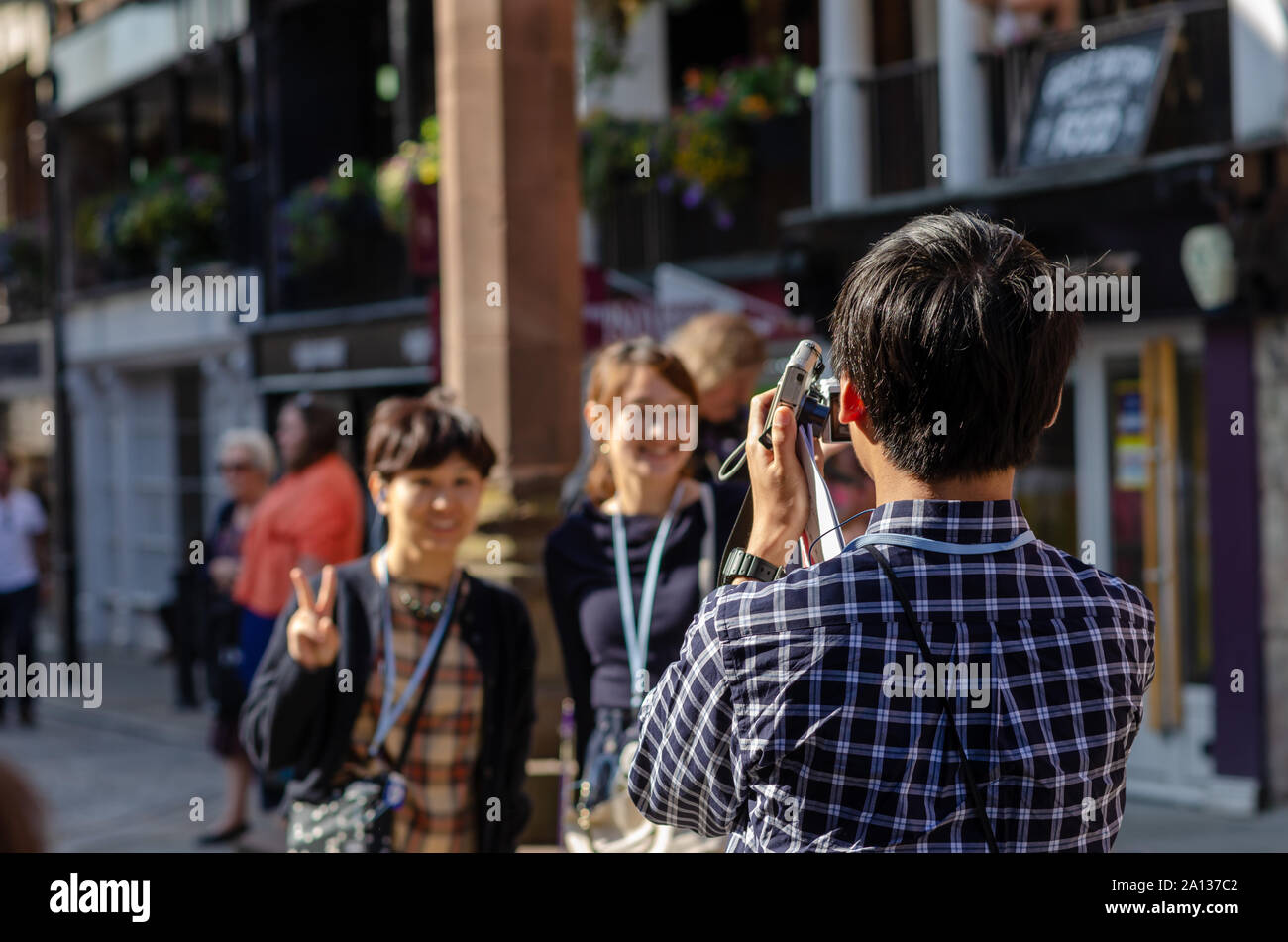 Young tourist from China taking photo of two smiling asian girls in the street of Chester, holding two photo cameras in his hand. Stock Photo