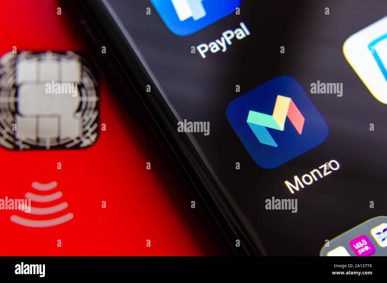 Monzo Bank app on the smartphone screen next to the Monzo debit card. Close up photo. Stock Photo