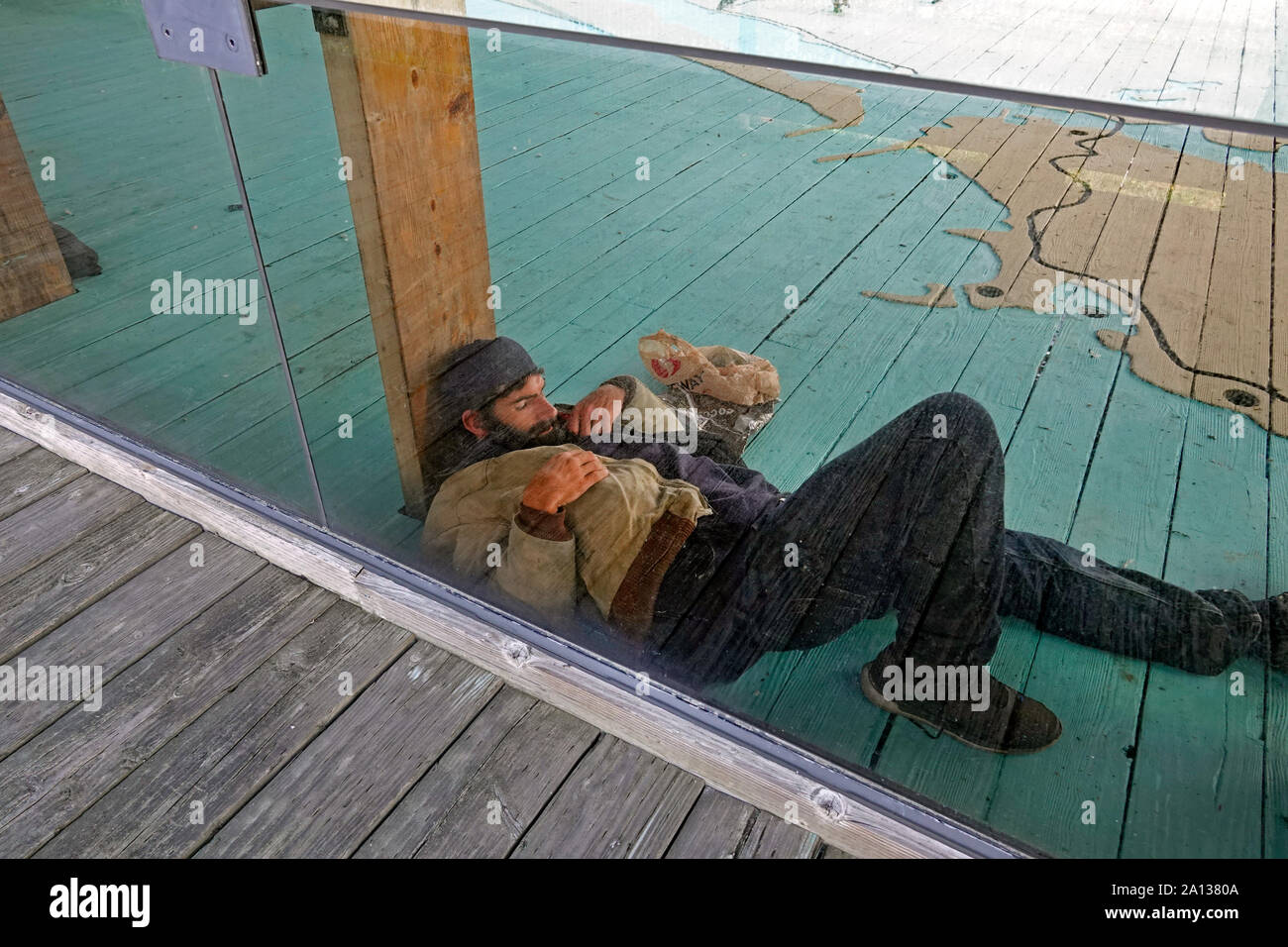 A homeless man sleeps behind a glass window at a public walkway in Coos Bay, Oregon, Along the Oregon Pacific Coast. Stock Photo