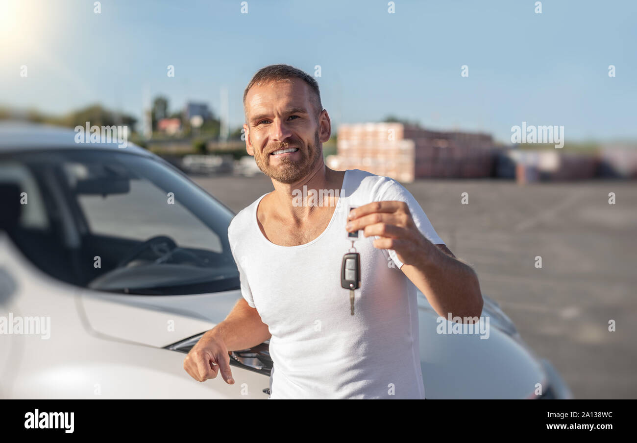 A male driver stands near a car with a key in his hand and smiles Stock