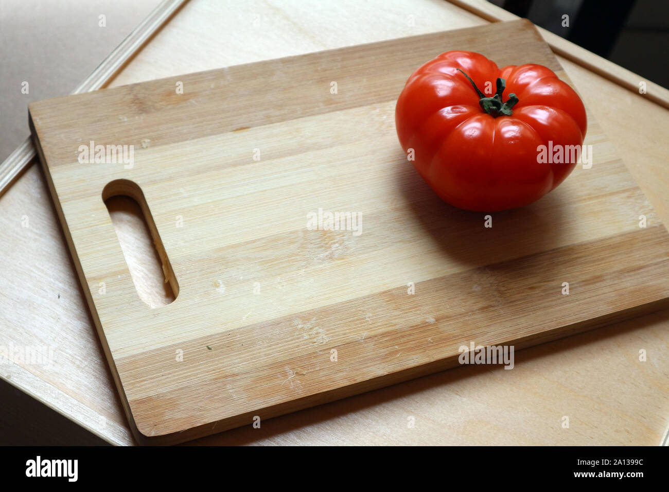 Single large ripe red whole tomatoes on chopping board Stock Photo
