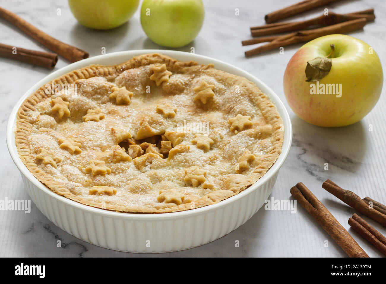 A traditional American apple pie decorated with stars and sugar, apples and cinnamon on a light background. Stock Photo