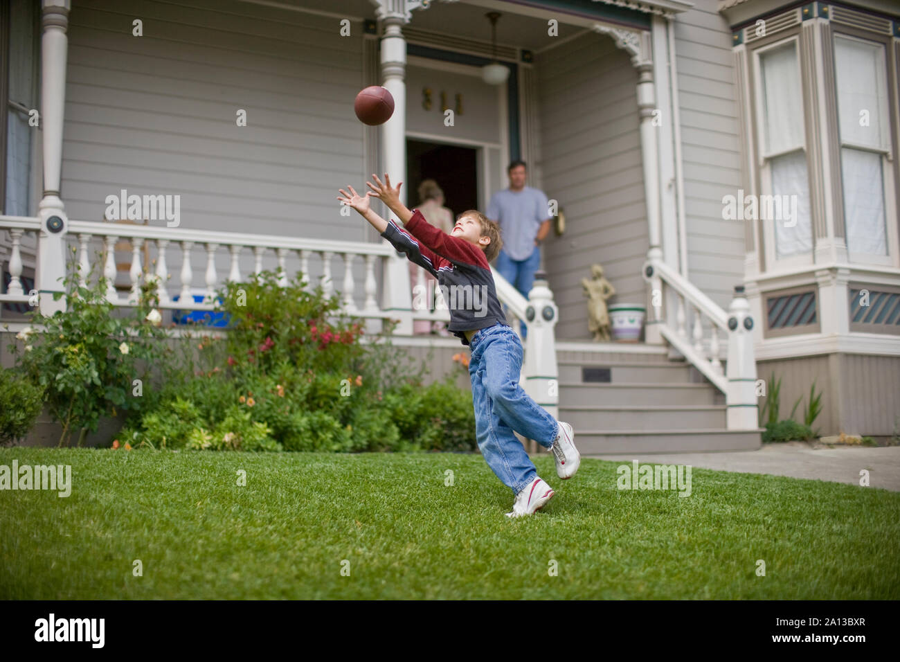Young boy reaching up to catch a football in the front yard of his home. Stock Photo