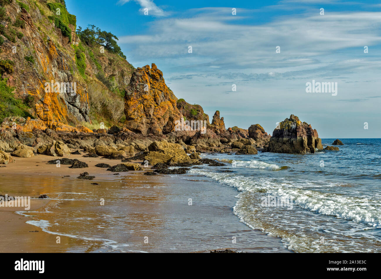 ROSEMARKIE TO CROMARTY WALK BLACK ISLE SCOTLAND LARGE YELLOW LICHEN CLAD SEA STACKS WITH WAVES BREAKING ON THE BEACH Stock Photo