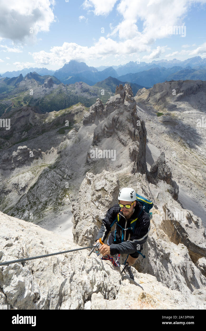 young handsome male climber on a steep and exposed rock face climbs a Via Ferrata in Alta Badia in the South Tyrol Stock Photo