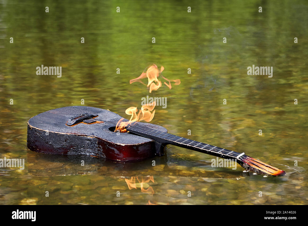 A burnt acoustic guitar with flames on its surface floats along the river. The musician set fire to the guitar and threw it into the river. A burning Stock Photo