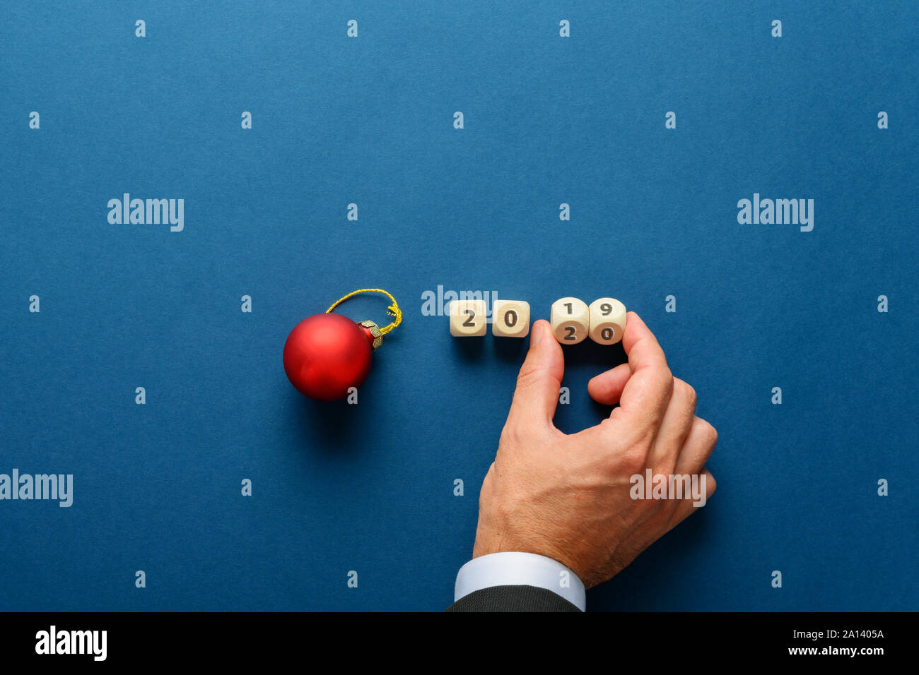 Red holiday bauble next to a 2019 sign on wooden dices with male hand turning the last two dices to change the date in 20120. Over navy blue backgroun Stock Photo