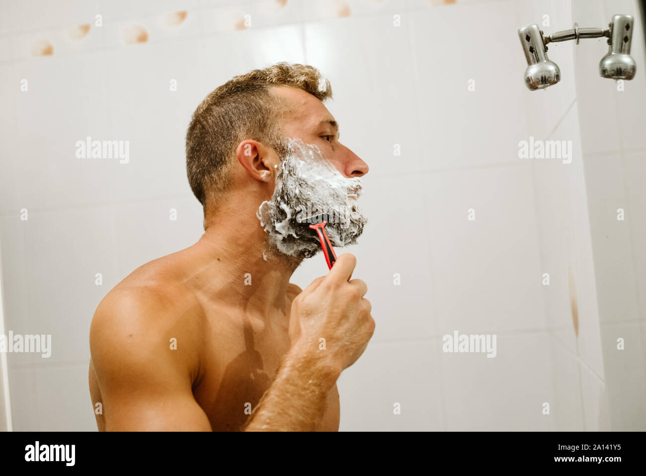 Man shaving face in bathroom mirror Stock Photo