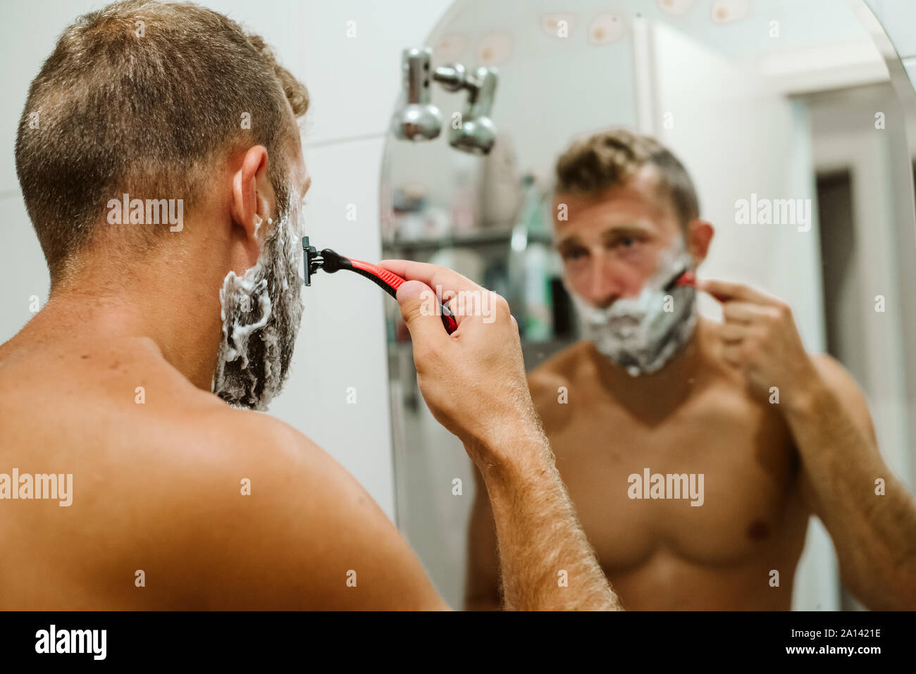 Man shaving face in bathroom mirror Stock Photo