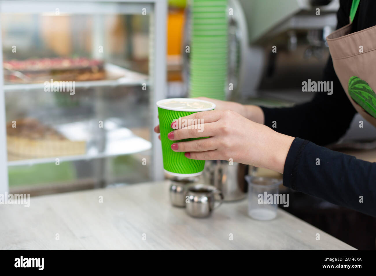 Barista gives the finished drink in a green eco-friendly paper cup to ...