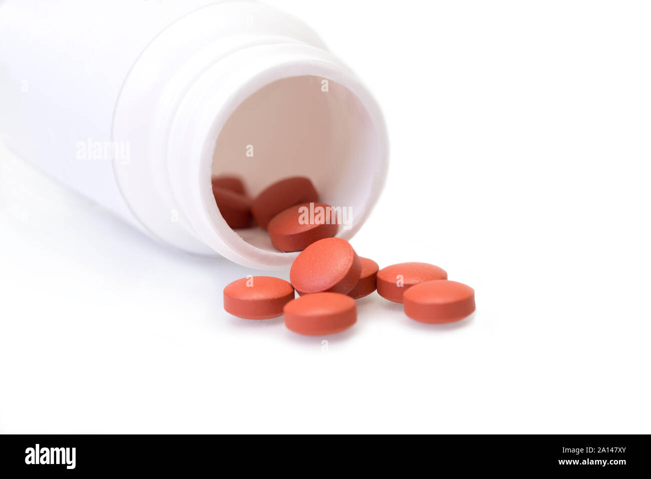 Red tablets spill from white medicine bottle on white. Stock Photo