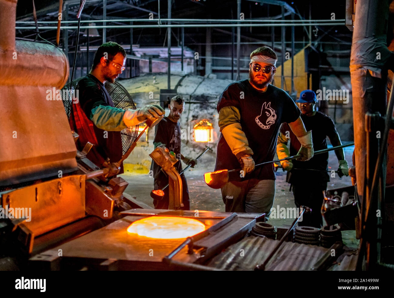 Sept 27 2019 Kokomo Indiana USA; workers at a North American glass factory, carry crucible ladles of melted glass. they then dump it onto a metal shee Stock Photo