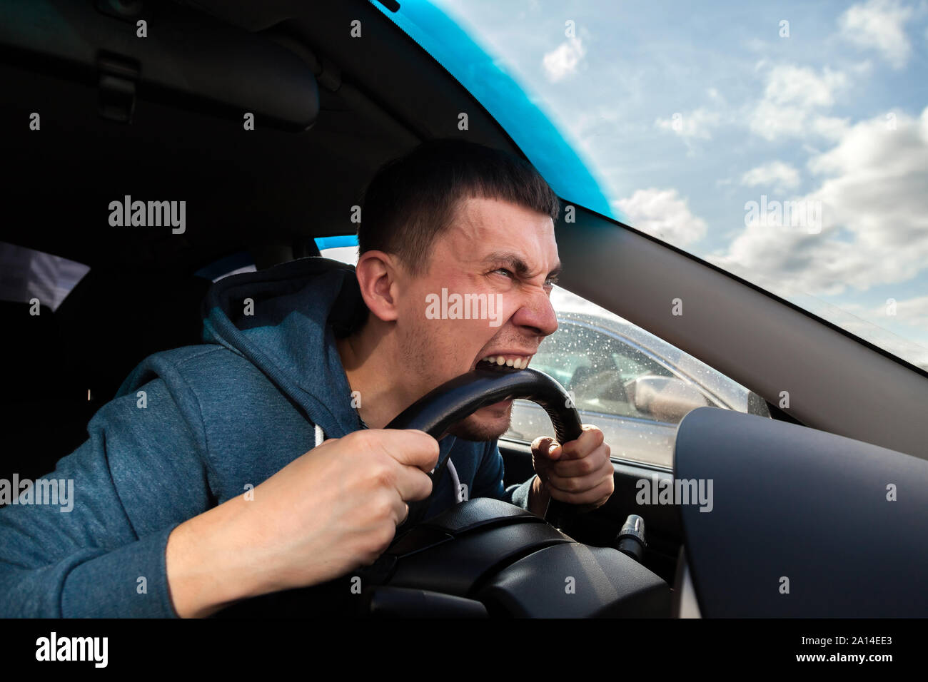 An unbalanced, goosey man bites a car steering wheel from