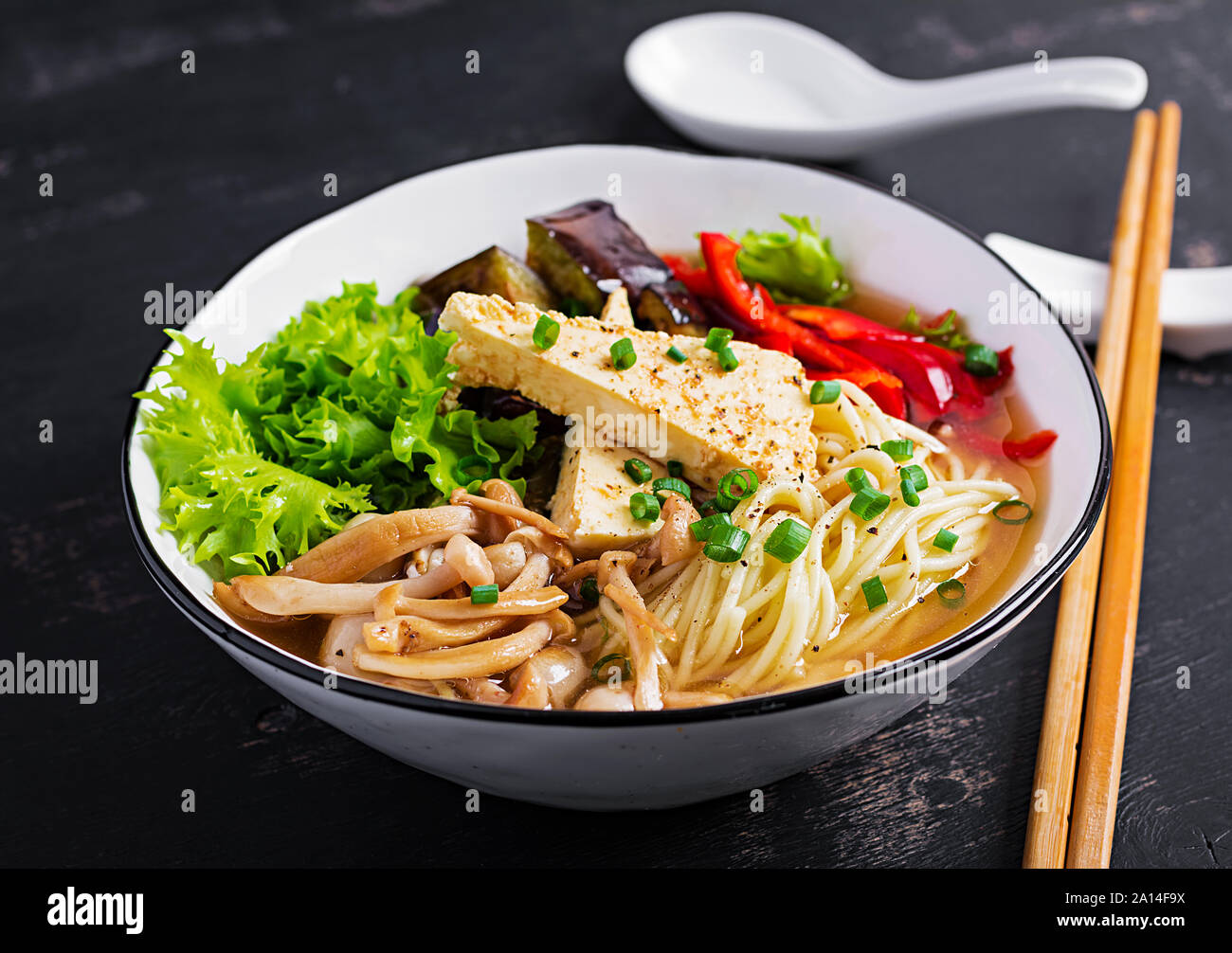 Asian vegan noodles soup with tofu cheese, shimeji mushrooms and fried eggplant in bowl on dark
