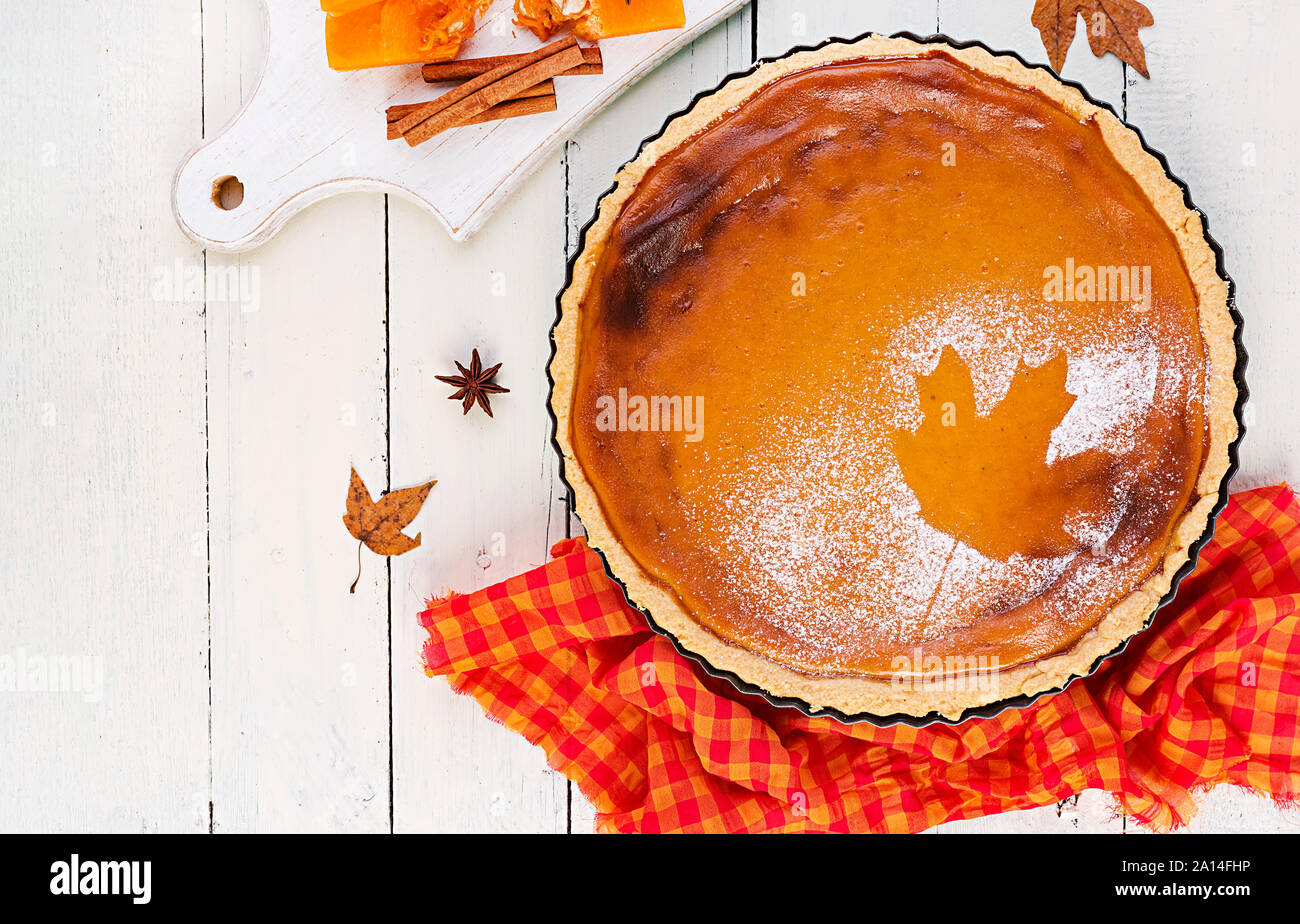 American homemade pumpkin pie with cinnamon and nutmeg, pumpkin seeds and autumn leaves on a white wooden table. Thanksgiving food. Top view. Flat lay Stock Photo