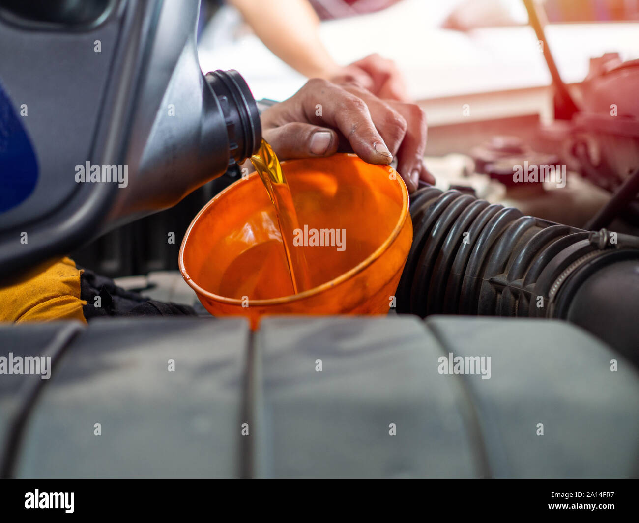Mechanic hand pouring fresh engine oil through orange funnel into the