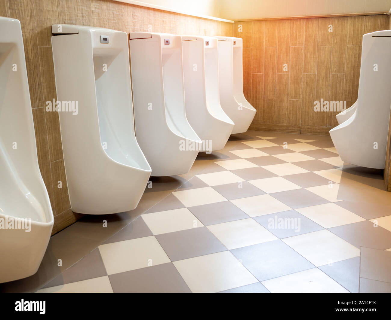 Row of modern luxury white automatic urinal for men on square tiles floor in earth tone toilet. Stock Photo