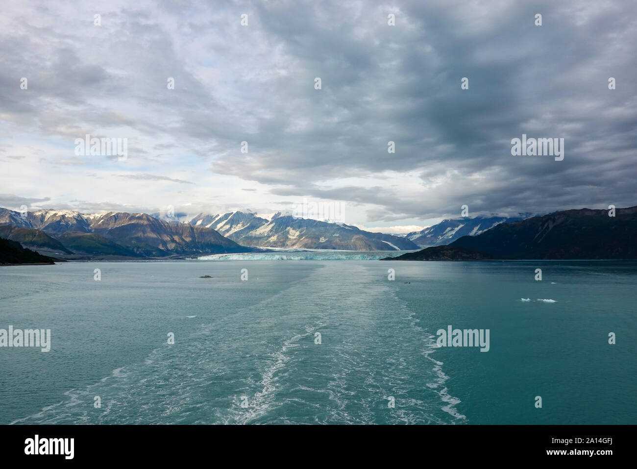 The wake of a cruise ship sailing away from Hubbard Glacier with a view of the glacier and mountains. Stock Photo