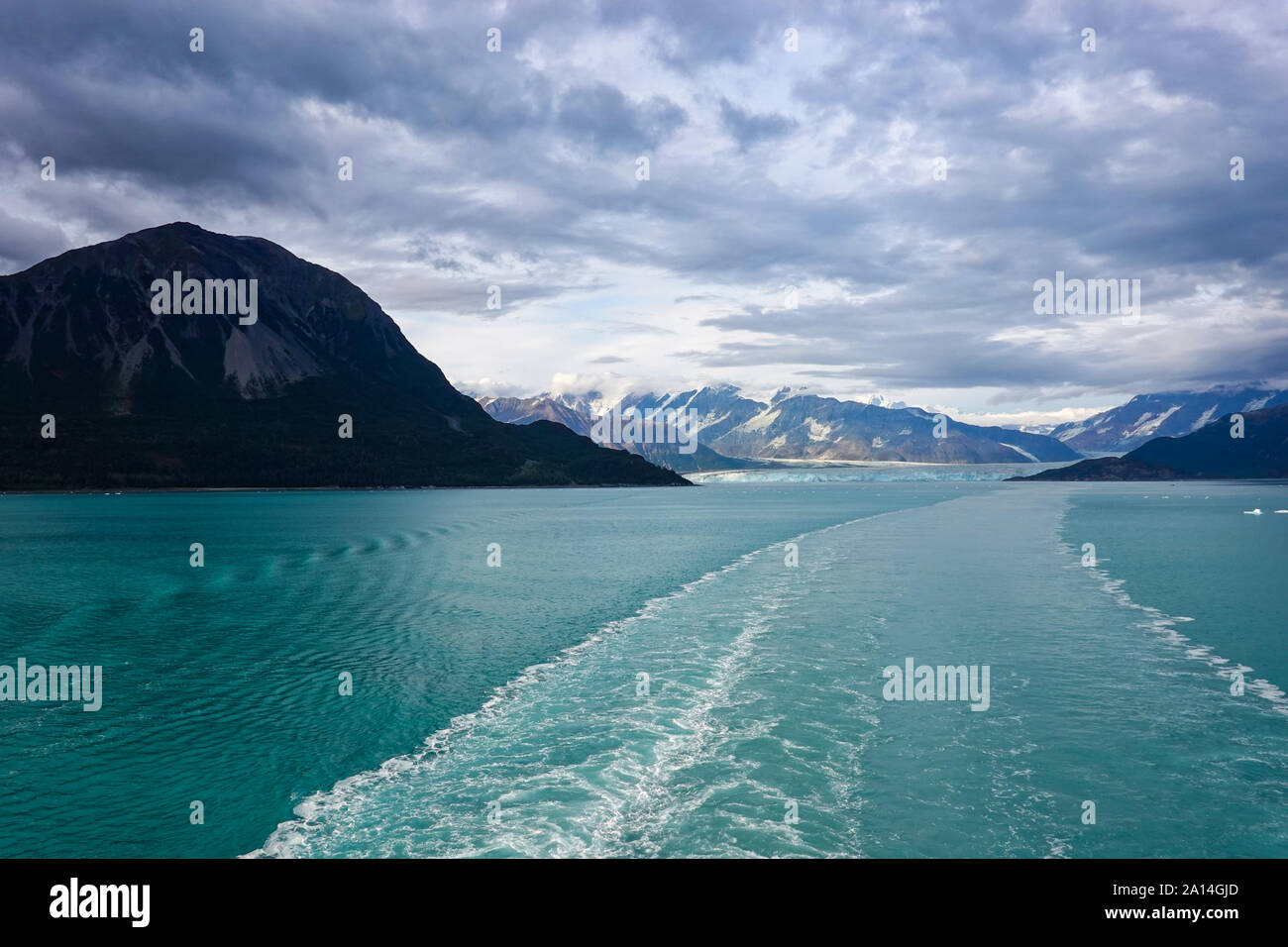 The wake of a cruise ship sailing away from Hubbard Glacier with a view of the glacier and mountains. Stock Photo