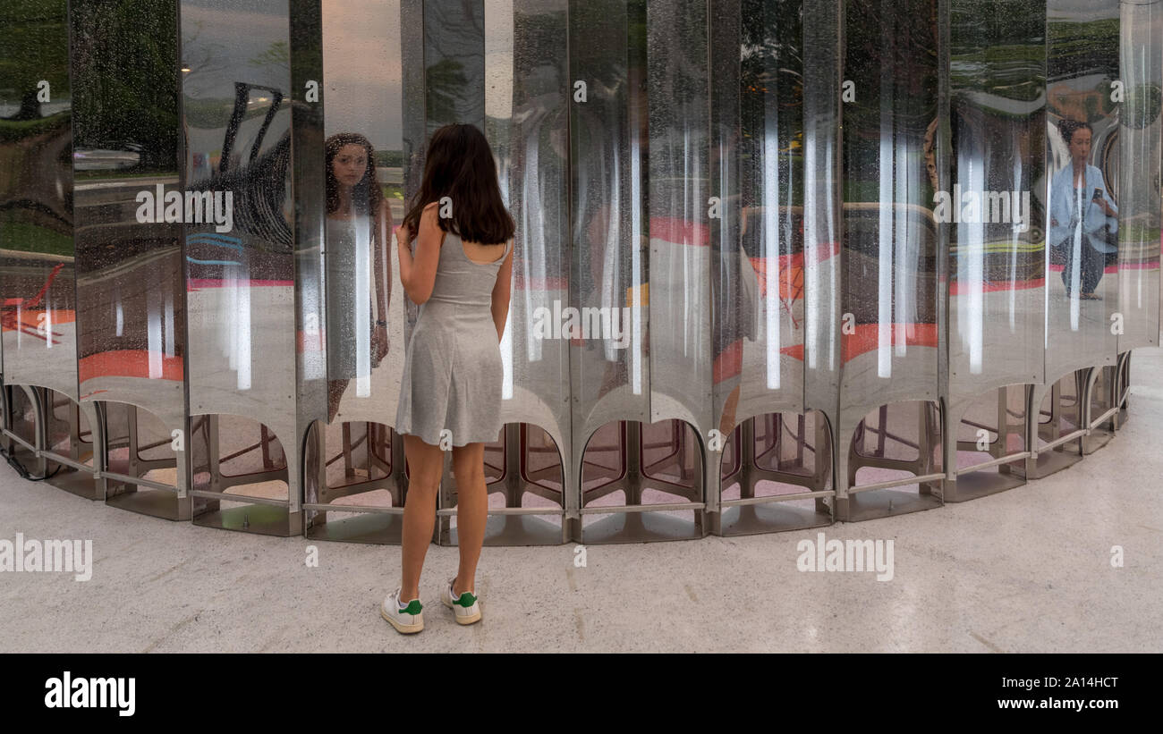 Teen in grey dress standing in front of multiple mirrors with back to camera Stock Photo