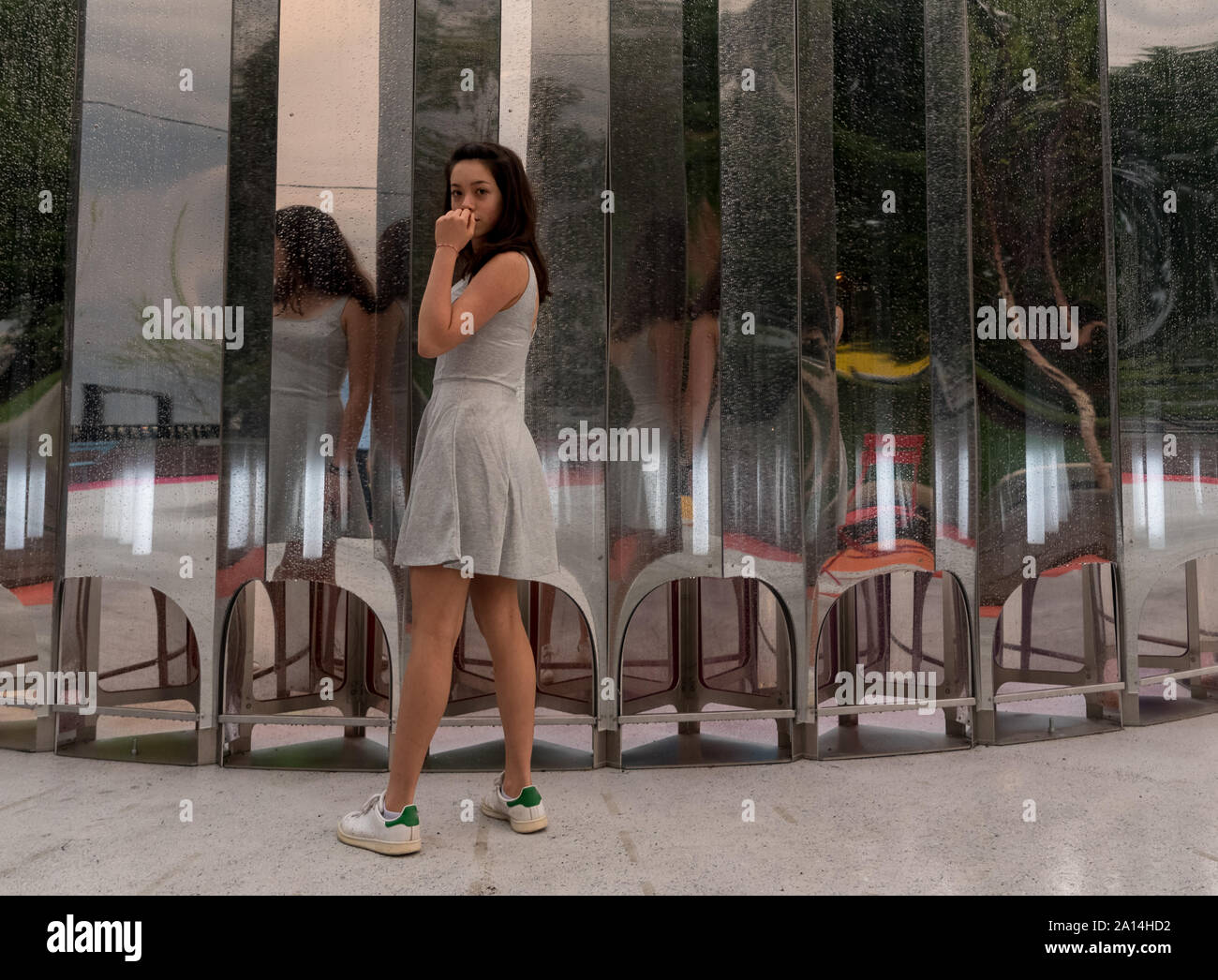 Teen in grey dress standing in front of multiple mirrors facing camera Stock Photo