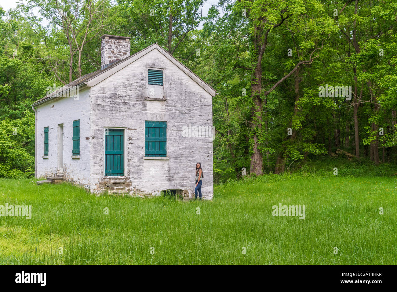 Woman standing by lock keepers white house with green shutters and door on the Chesapeake and Ohio Canal Stock Photo