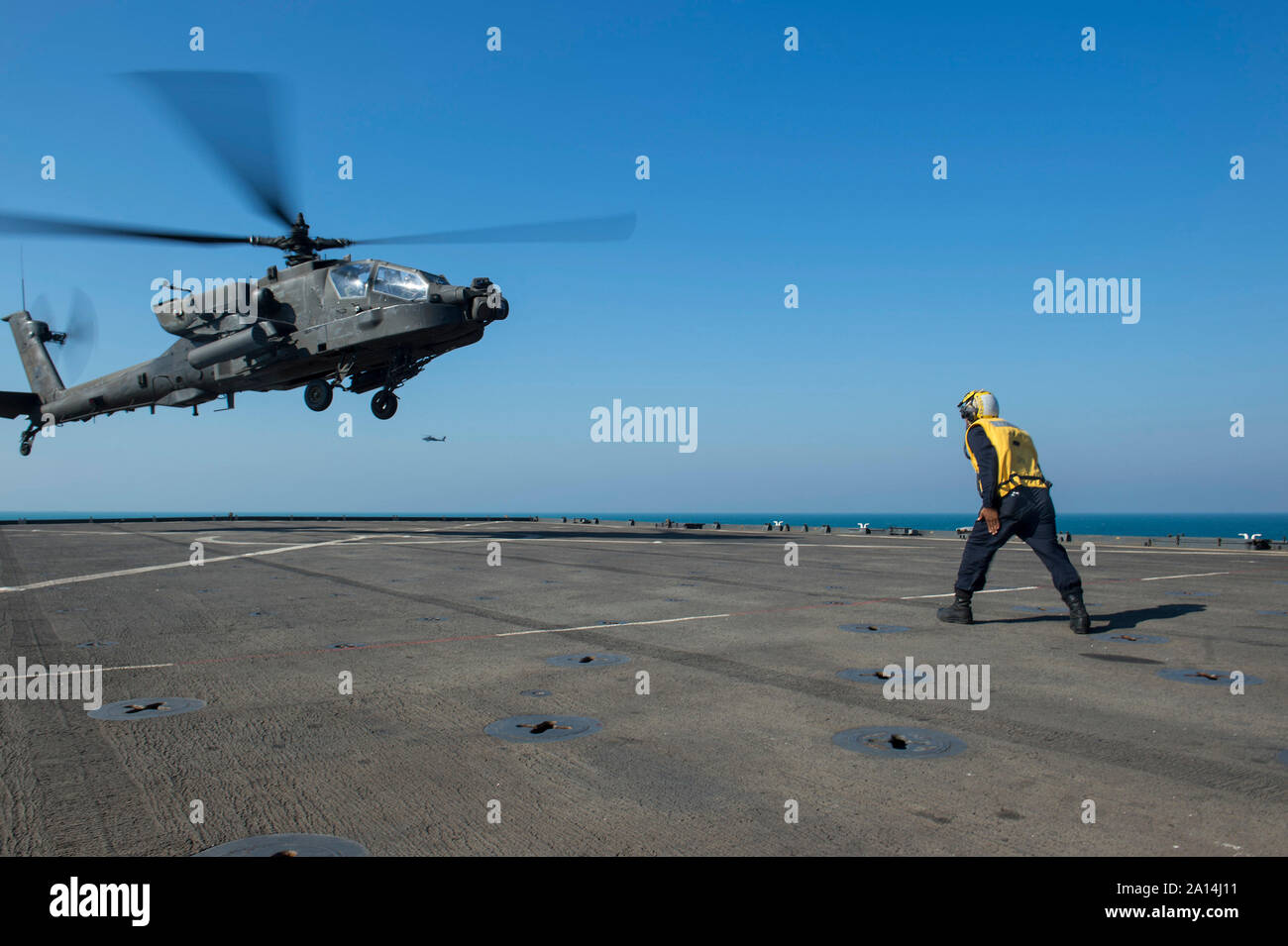 Boatswain's Mate signals an Army Apache helicopter on the flight deck of USS Comstock. Stock Photo