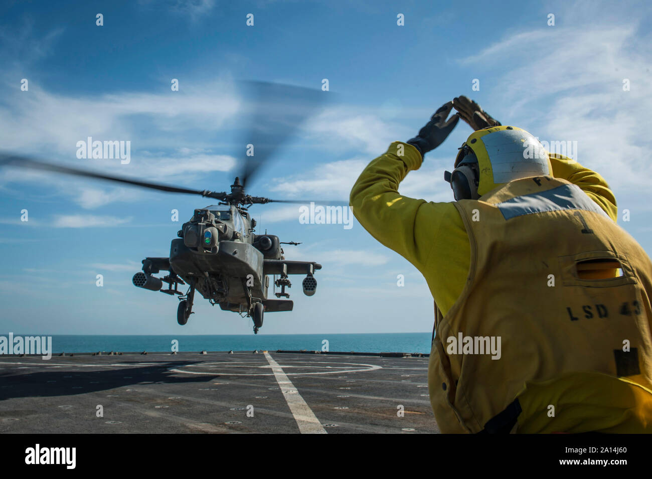 Boatswain's Mate signals an AH-64 Apache helicopter aboard USS Fort McHenry. Stock Photo