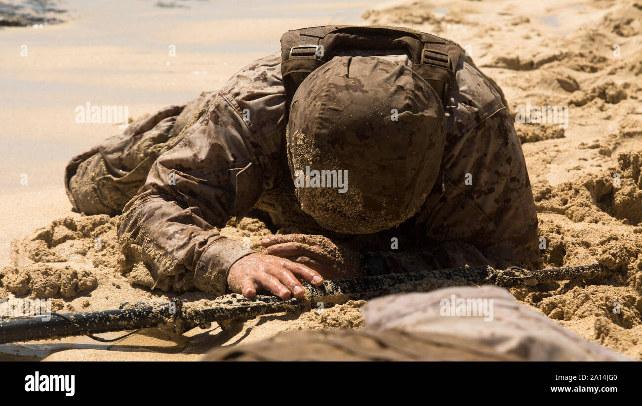 A U.S. Marine low crawls through an obstacle course. Stock Photo