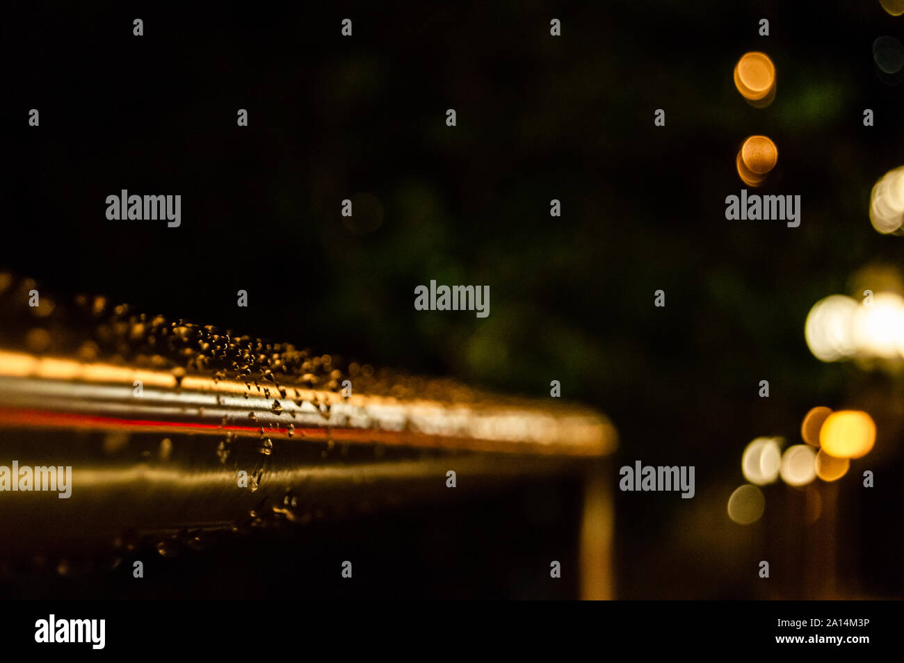 A handrail is covered in raindrops at night. Shallow focus. Copy space background. Stock Photo