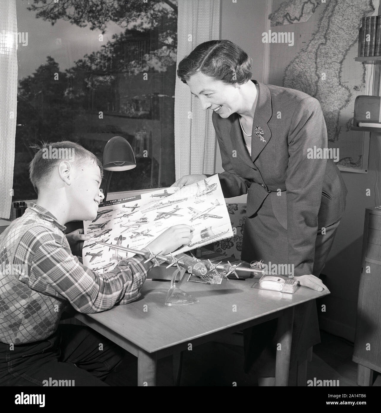 Hobby in the 1950s. A boy is sitting at a table with a plastic model of an American bomb aircraft B29. It's made by the American manufacturer of plastic models Aurora Plastics coporation. The company specialized in plane models and had it's most success with them in the 1950s and 1960s. At this time, building models of planes and cars was a very popular hobby. Sweden 1956 ref 3091 Stock Photo