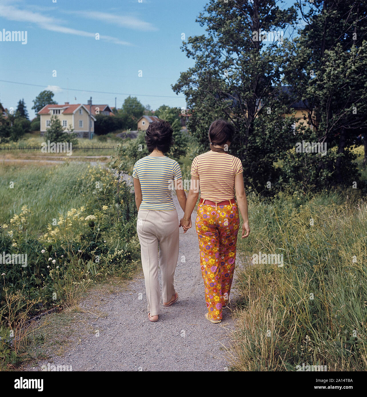 Livsstil på 1960-talet. Två kvinnor går hand i hand en sommardag. Härligt 60-tals blommigt mönster på byxorna. Sverige 1960-tal Stock Photo