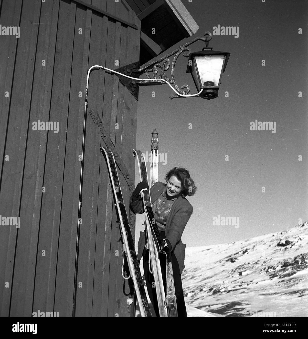 Winter in the 1940s. A young woman is preparing her skis and uses a seal skin underneath the skis to be able to climb the snowy mountain tops and not slide backwards. Sweden 1943. Kristoffersson Ref D70-4 Stock Photo