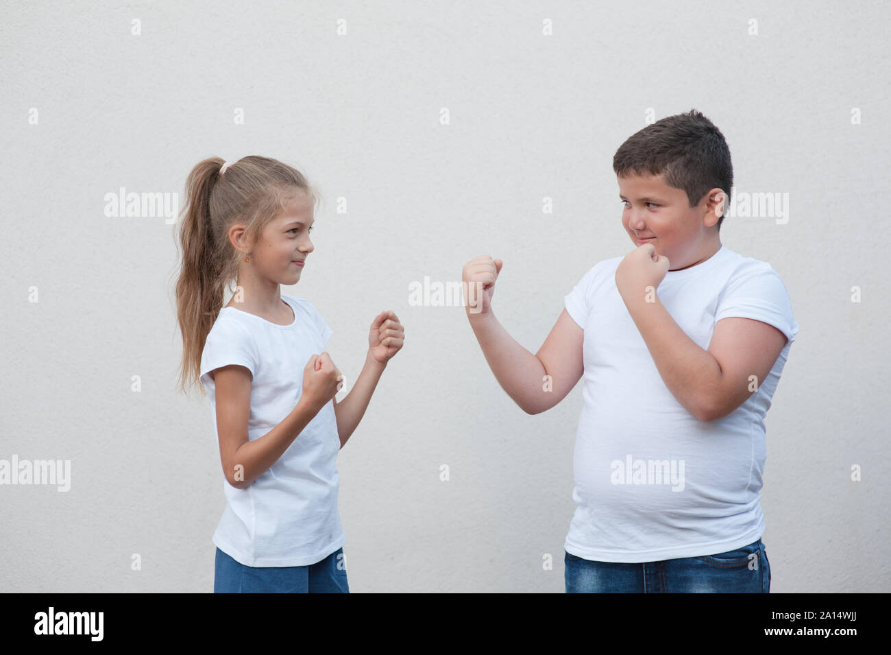 gender issues concept of two kids little thick boy against small thin girl holding fist ready to fight Stock Photo